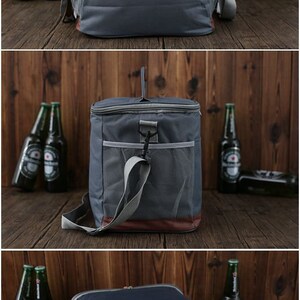 May include: A gray canvas cooler bag with brown leather accents and a mesh pocket. The cooler bag has a top handle and a shoulder strap. The cooler bag is sitting on a wooden surface.