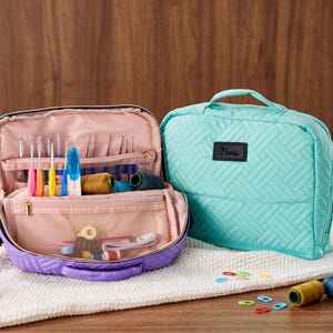 May include: A quilted storage case in light purple and teal, featuring a top handle and zipper closure. The open case reveals a light pink interior with mesh pockets and elastic loops holding various colorful crochet hooks and sewing thread spools.