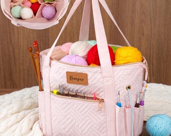 May include: A light pink quilted yarn storage bag with a top handle and a front zippered pocket. The bag features a brown leather-like patch with the text Kemper, multiple exterior side pockets for crochet hooks, and an interior divider filled with various colorful yarn balls.