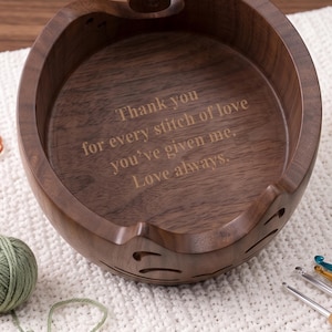 May include: A round dark brown wooden yarn bowl with a spiral cutout on the rim and decorative side slits. The interior base is engraved with the text: Thank you for every stitch of love you've given me. Love always. The bowl has a smooth finish.
