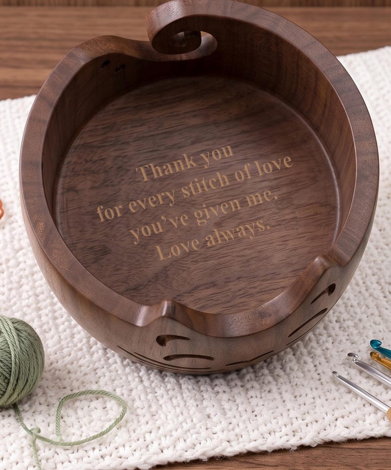 May include: A round dark brown wooden yarn bowl with a spiral cutout on the rim and decorative side slits. The interior base is engraved with the text: Thank you for every stitch of love you've given me. Love always. The bowl has a smooth finish.