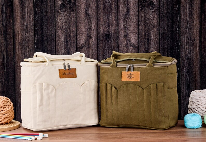 May include: Two canvas tote bags, cream and olive green, with top handles and front pockets. Each bag has a leather patch with text or a design. The cream bag has the name "Matthew" on it.