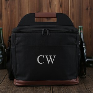 May include: Black canvas cooler bag with a brown leather handle and trim. The cooler bag has a zipper closure and a monogrammed "CW" on the front.