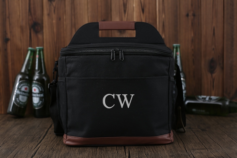 May include: Black canvas cooler bag with a brown leather handle and trim. The cooler bag has a zipper closure and a monogrammed "CW" on the front.