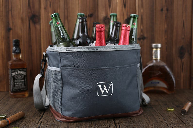 May include: A gray insulated cooler bag with a brown leather trim and a white "W" monogram. The cooler bag is filled with various beer and wine bottles.