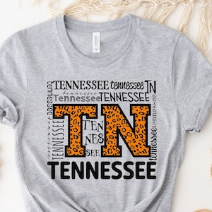 May include: Gray t-shirt with a graphic of the letter "T" in a leopard print design. The letter is surrounded by the word "Tennessee" repeated multiple times in black text.