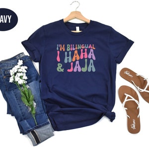 May include: A navy blue t-shirt with the text "I'm Bilingual I Haha & Jaja" in colorful, retro-style lettering.