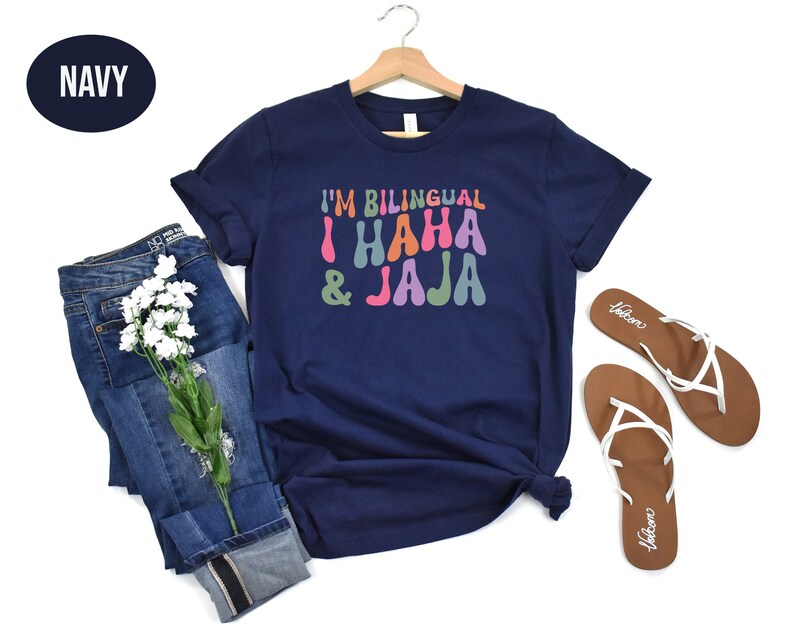 May include: A navy blue t-shirt with the text "I'm Bilingual I Haha & Jaja" in colorful, retro-style lettering.