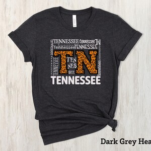 May include: Dark grey heather t-shirt with a white graphic of the word "Tennessee" with the letters "TN" in orange and a leopard print pattern.