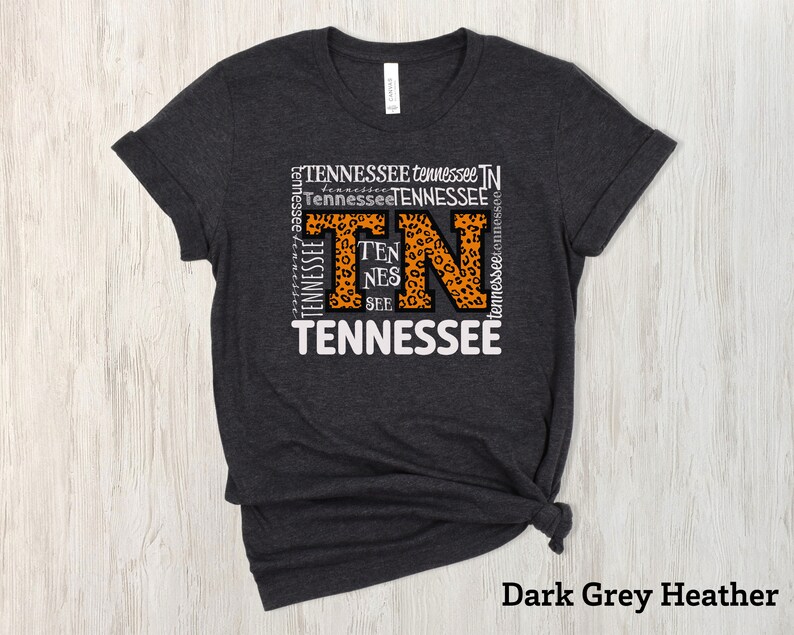 May include: Dark grey heather t-shirt with a white graphic of the word "Tennessee" with the letters "TN" in orange and a leopard print pattern.