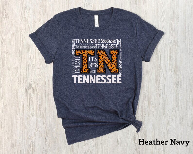 May include: Heather navy blue t-shirt with a white graphic of the letters "TN" in a leopard print design. The letters are surrounded by the word "Tennessee" repeated multiple times.