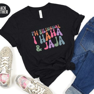 May include: Black heather t-shirt with the text "I'm Bilingual I Haha & Jaja" in colorful, retro-style lettering.