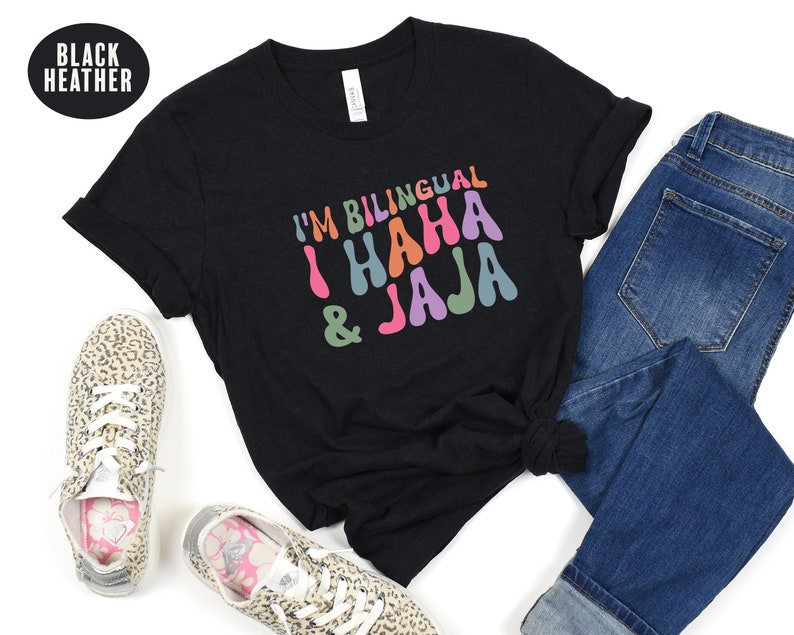 May include: Black heather t-shirt with the text "I'm Bilingual I Haha & Jaja" in colorful, retro-style lettering.