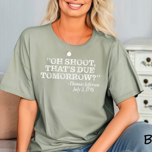 May include: Sage green t-shirt with a white graphic print that reads "OH SHOOT, THAT'S DUE TOMORROW?" -Thomas Jefferson July 3, 1776