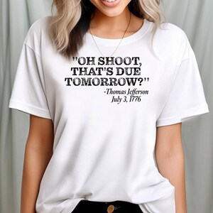 May include: White t-shirt with a black graphic print that reads "OH SHOOT, THAT'S DUE TOMORROW?" -Thomas Jefferson July 3, 1776