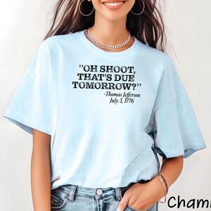 May include: Light blue t-shirt with a black graphic print that reads "OH SHOOT, THAT'S DUE TOMORROW?" -Thomas Jefferson July 3, 1776