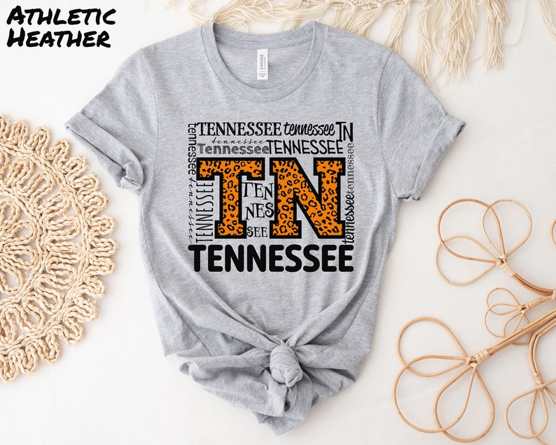 May include: Gray t-shirt with a graphic of the letter "T" in a leopard print design. The letter is surrounded by the word "Tennessee" repeated multiple times in black text.