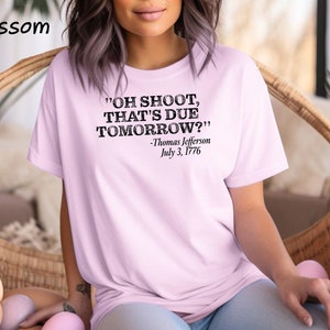 May include: A pink t-shirt with a black graphic print that reads "OH SHOOT, THAT'S DUE TOMORROW?" -Thomas Jefferson July 3, 1776.