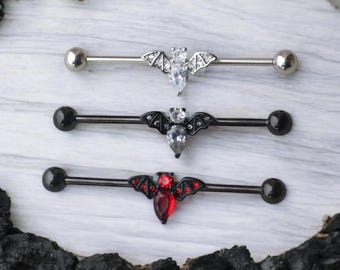 May include: Three different styles of barbell piercings with a bat design. The top barbell is silver with a clear crystal, the middle barbell is black with a clear crystal, and the bottom barbell is black with a red crystal.