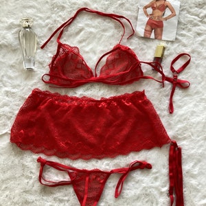 May include: Red lace lingerie set with a bra, skirt, and garter belt. The set is laid out on a white fluffy surface.