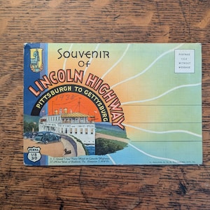 May include: A vintage postcard titled Souvenir of Lincoln Highway Pittsburgh to Gettysburg featuring a graphic of the Grand View Point Hotel, a dark car, and the text Penna US 30. The background has a sunburst design and lines for writing.
