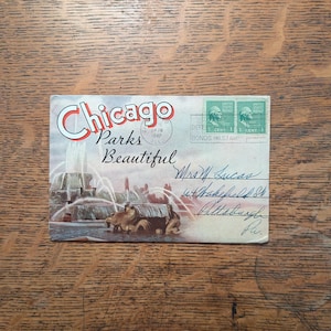 May include: A vintage postcard featuring a color illustration of a Chicago fountain with the text Chicago Parks Beautiful. It includes two green one-cent United States postage stamps, a postmark dated 1949, and handwritten address details in blue ink.