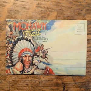 May include: Vintage postcard featuring a Native American chief in full headdress, with the text "The Mohawk Trail" in red and blue. The postcard also includes the text "Thru the Berkshires Mass." and a postage stamp area.