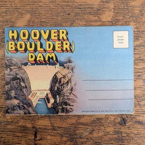 May include: Vintage postcard featuring the Hoover Dam, with the text "HOOVER (BOULDER) DAM" in yellow and orange lettering. The image shows the dam structure, water, and surrounding landscape under a blue sky. A place for a stamp is visible.