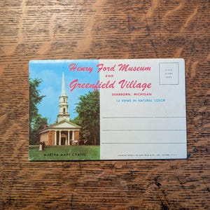 May include: Vintage postcard featuring the Martha Mary Chapel at the Henry Ford Museum and Greenfield Village in Dearborn, Michigan. The postcard has a color image of the chapel with a tall steeple, surrounded by trees, and text that reads "14 Views in Natural Color."
