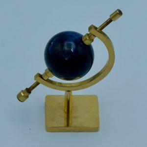 May include: A small brass globe with a blue marble sphere on a stand. The globe is tilted at an angle and the stand has a square base.