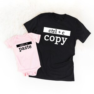May include: A black t-shirt with the text "ctrl + c copy" in white and a pink baby bodysuit with the text "ctrl + v paste" in black.