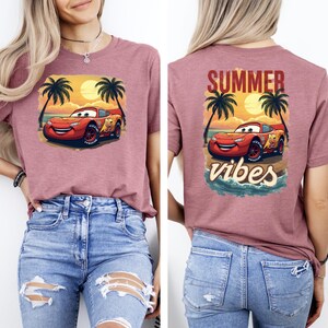 Gray t-shirt with Lightning McQueen in front of sunset and palm trees, back print says “Summer Vibes.” Perfect Pixar Cars beach shirt for vacations and summer fun.