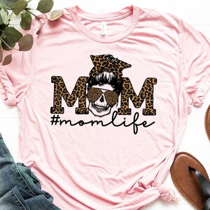 May include: Pink t-shirt featuring a black and brown leopard print "MOM" graphic with a skull wearing sunglasses and a headband. The text "#momlife" is below the graphic.