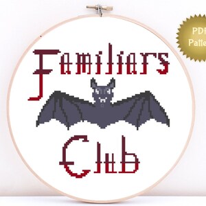 May include: A white embroidery hoop with the text "Familiars Club" in red, featuring a black bat with red eyes. The text "PDF Pattern" is on a gold star sticker.