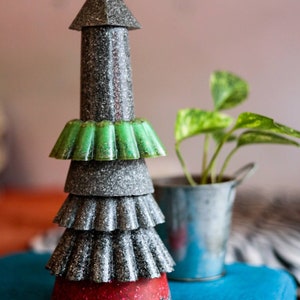 May include: A tiered Christmas tree decoration made from repurposed cupcake liners. The tree is silver with green and red accents.
