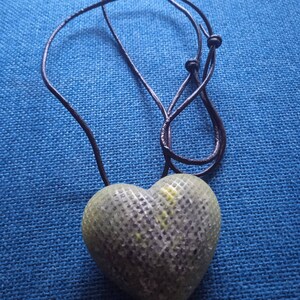 May include: A green heart-shaped pendant with a textured surface hangs from a black cord.