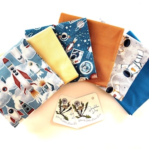 May include: A collection of colorful fabric squares with space-themed and solid designs. The fabrics feature rockets, astronauts, planets, and stars in shades of blue, orange, yellow, and gray. Two small tags with botanical illustrations are also present.