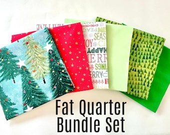 May include: A set of six fat quarter fabric squares featuring a Christmas theme. The fabrics include a red fabric with white stars, a green fabric with white triangles, a green fabric with white trees, a light green fabric with a white Christmas message, a blue fabric with white trees and white stars, and a solid green fabric.