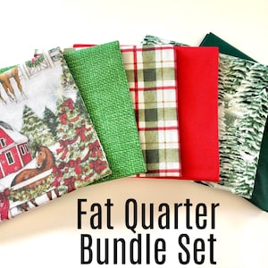 May include: A fat quarter bundle set featuring various fabric patterns. The fabrics include a red barn scene, green textured, plaid, solid red, winter forest, and solid dark green. The text "Fat Quarter Bundle Set" is displayed.