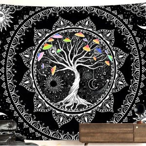 May include: Black and white tapestry featuring a central tree design with colorful mushroom-like shapes. The tree is surrounded by a circular mandala pattern, sun, moon, and stars. The tapestry is hanging on a wall above a wooden cabinet.