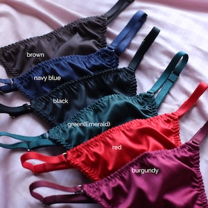 May include: A collection of six satin-finish undergarments with adjustable straps, arranged in a row. The colours are labelled as brown, navy blue, black, green (emerald), red, and burgundy. Each piece features a gathered, elasticised top edge.