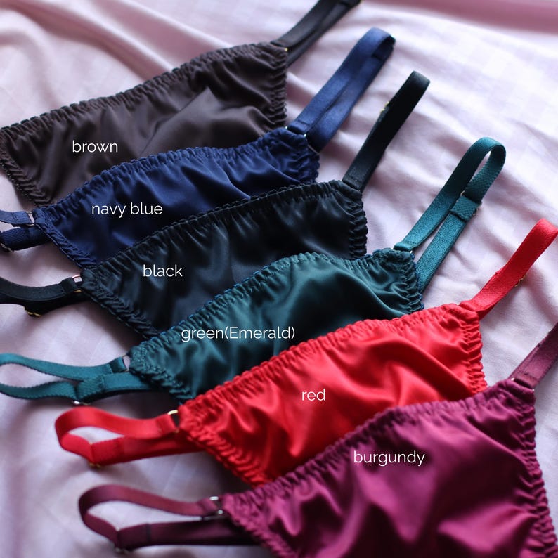 May include: A collection of six satin-finish undergarments with adjustable straps, arranged in a row. The colours are labelled as brown, navy blue, black, green (emerald), red, and burgundy. Each piece features a gathered, elasticised top edge.