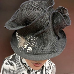 May include: A black, wide-brimmed hat with a ruffled crown and a small feather accent. The hat is made of a woven material and has a slightly textured surface.