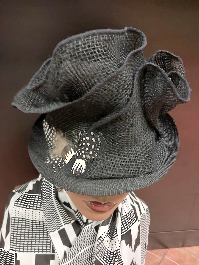 May include: A black, wide-brimmed hat with a ruffled crown and a small feather accent. The hat is made of a woven material and has a slightly textured surface.