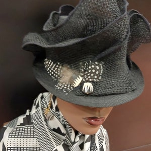 May include: A black, ruffled hat with a white and black feather accent. The hat is worn on a mannequin with a black and white patterned scarf.