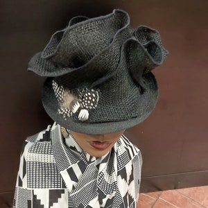 May include: A black, ruffled, wide-brimmed hat with a small, white, polka-dotted feather accent.