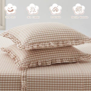 Pu&ograve; includere: Due cuscini rettangolari e un lenzuolo abbinato con motivo a quadretti vichy marrone chiaro e bianco. Ogni cuscino presenta un bordo arricciato. Sopra, quattro icone con il testo: Ultra Soft, Skin Friendly, Breathable, Machine Washable.