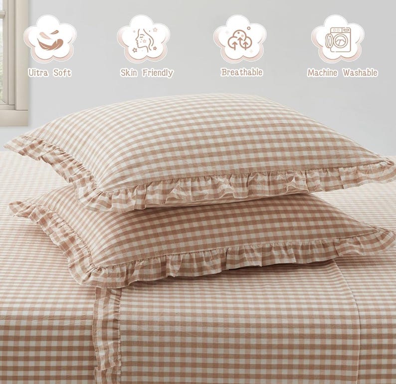 Pu&ograve; includere: Due cuscini rettangolari e un lenzuolo abbinato con motivo a quadretti vichy marrone chiaro e bianco. Ogni cuscino presenta un bordo arricciato. Sopra, quattro icone con il testo: Ultra Soft, Skin Friendly, Breathable, Machine Washable.