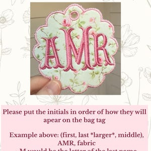 Op de afbeelding: Een cirkelvormig stoffen taslabel met een geschulpte rand, een lichtgroene achtergrond en een roze bloemenpatroon. Het label is geborduurd met de roze initialen AMR in een groot lettertype. De tekst op de afbeelding luidt: When placing your order: Please put the initials in order of how they will apear on the bag tag Example above: (first, last *larger*, middle), AMR, fabric ^ M would be the letter of the last name.