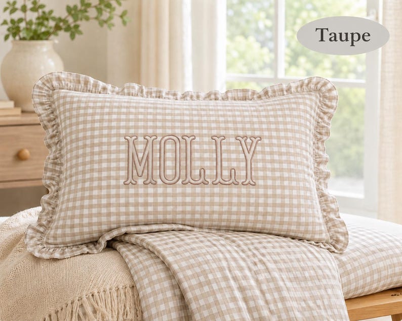 Pu&ograve; includere: Un cuscino rettangolare con motivo a quadretti vichy color tortora e bianco e bordo arricciato. Al centro del cuscino &egrave; ricamato il nome MOLLY con filo color tortora. Il cuscino &egrave; presentato insieme a una coperta a quadretti abbinata.